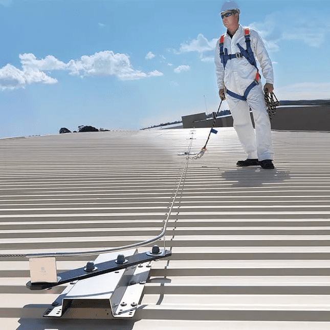 Static line roof safety system in use: A worker is connected by harness to the stainless steel static line while working on a sloping corrugated roof